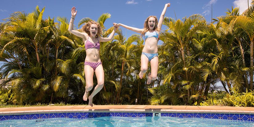 Two teen girls jumping into swimming pool